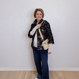 Woman standing against a white wall holding a gold handbag.