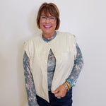 Woman wearing a cream vest over a patterned shirt with a plain background