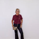 Woman wearing a burgundy top and black pants, standing against a white wall.