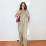 Woman in a green outfit holding a red bag against a white wall.