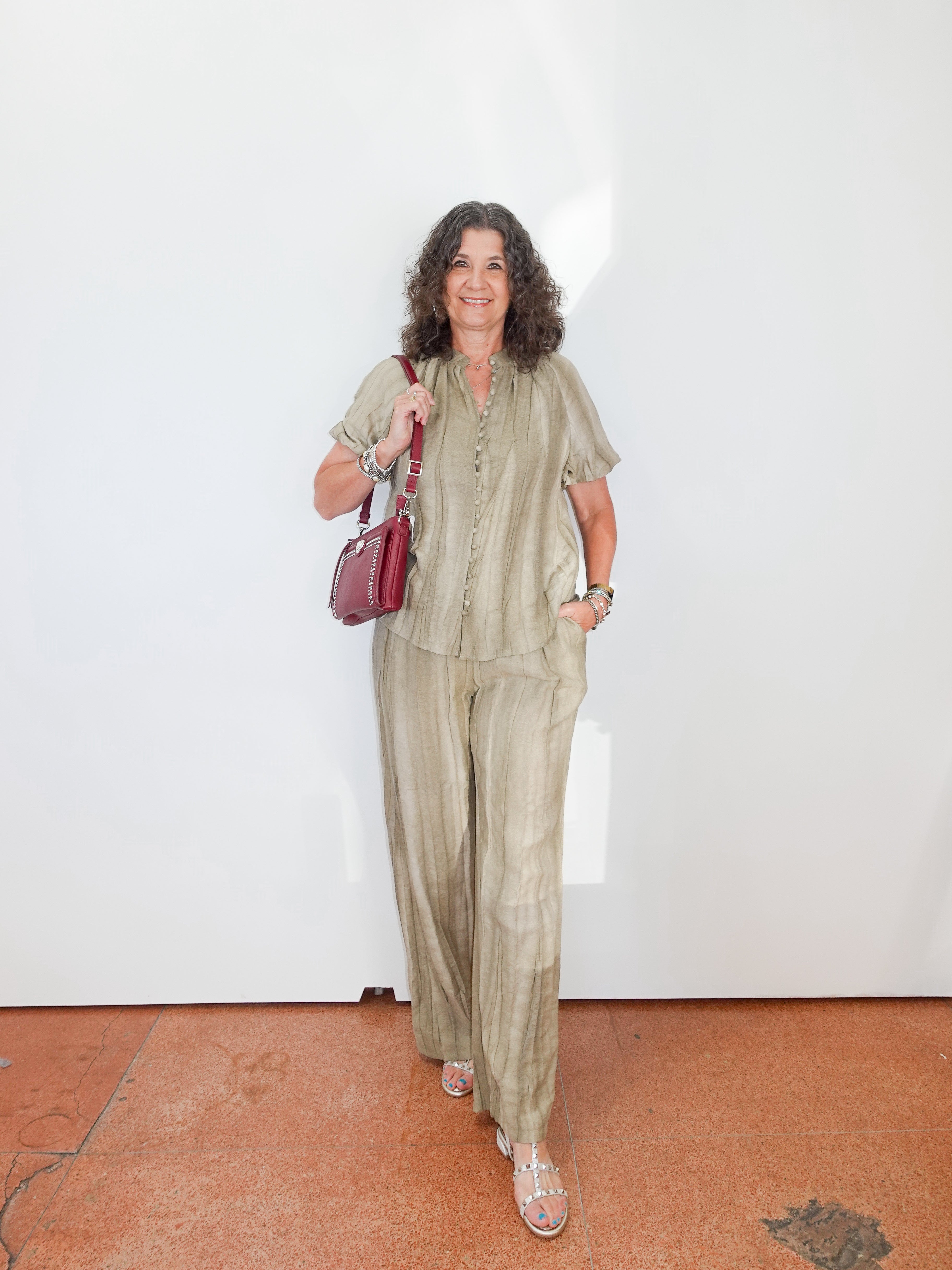 Woman in a green outfit holding a red bag against a white wall.