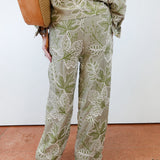 Person wearing a green and white leaf-patterned outfit with a brown bag on a white background.