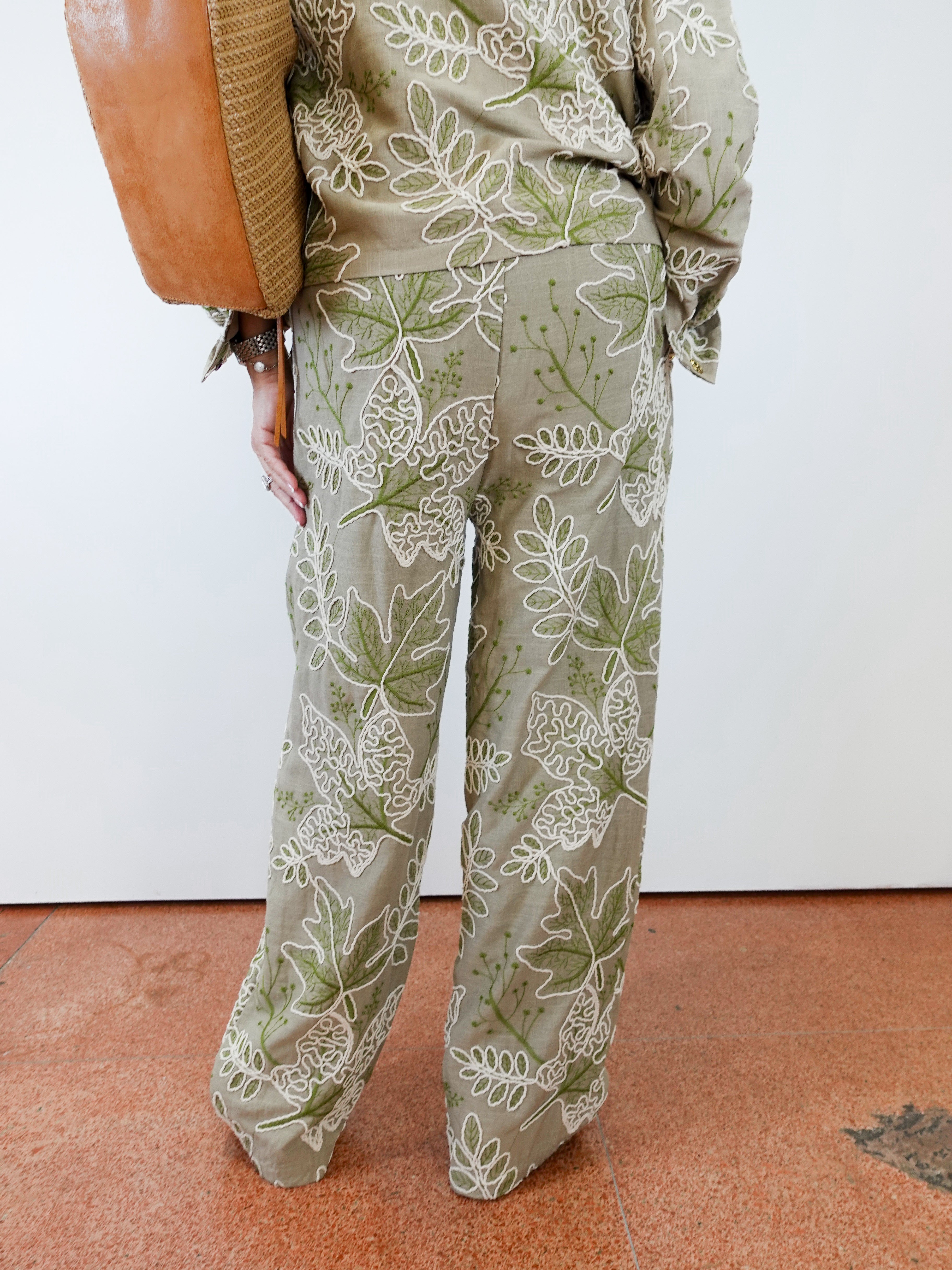 Person wearing a green and white leaf-patterned outfit with a brown bag on a white background.