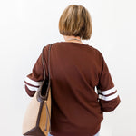 Person wearing a brown sweater with white stripes on sleeves, holding a beige handbag.