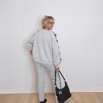 Person wearing a gray tracksuit holding a black handbag against a white wall.