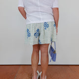 Person wearing a white shirt and patterned skirt with a blue clutch against a plain background
