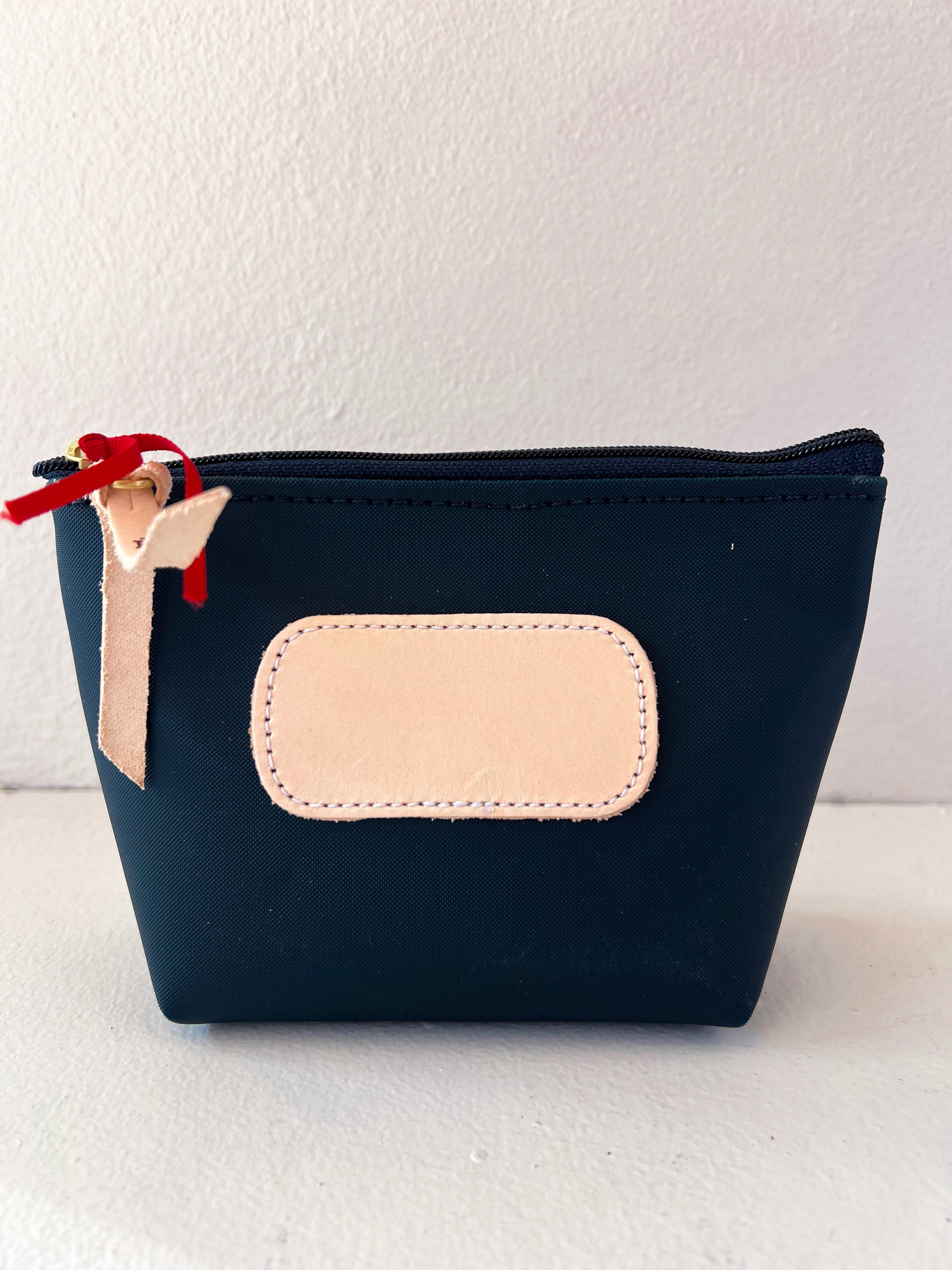 Navy blue pouch with beige patch and red zipper pull on a white background