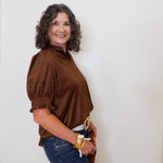 Woman wearing a brown blouse and blue jeans against a white wall