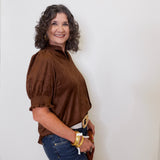 Woman wearing a brown blouse and blue jeans against a white wall