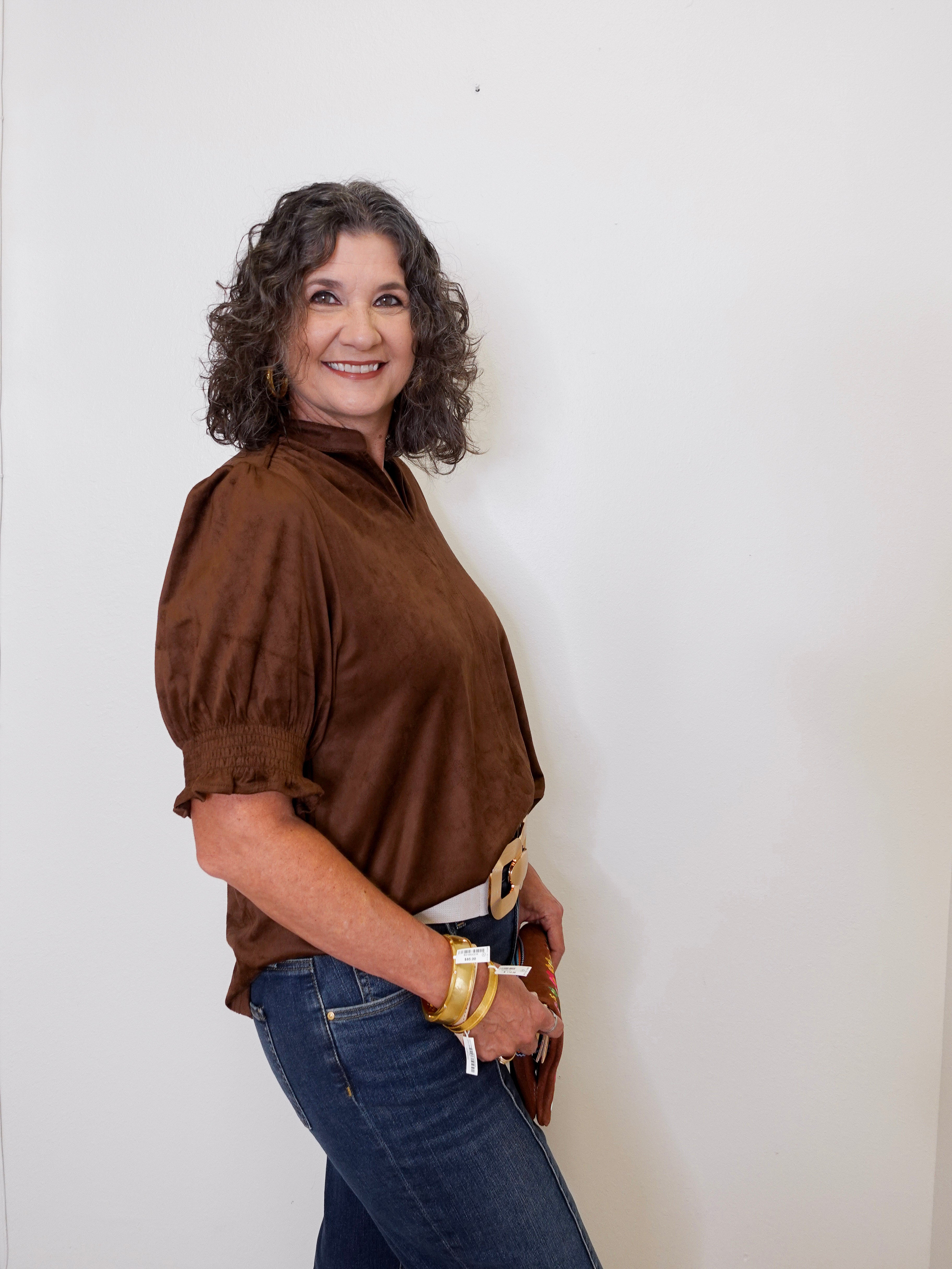 Woman wearing a brown blouse and blue jeans against a white wall