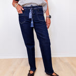 Person wearing dark blue jeans and a striped shirt against a white wall.