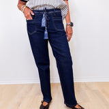 Person wearing dark blue jeans and a striped shirt against a white wall.