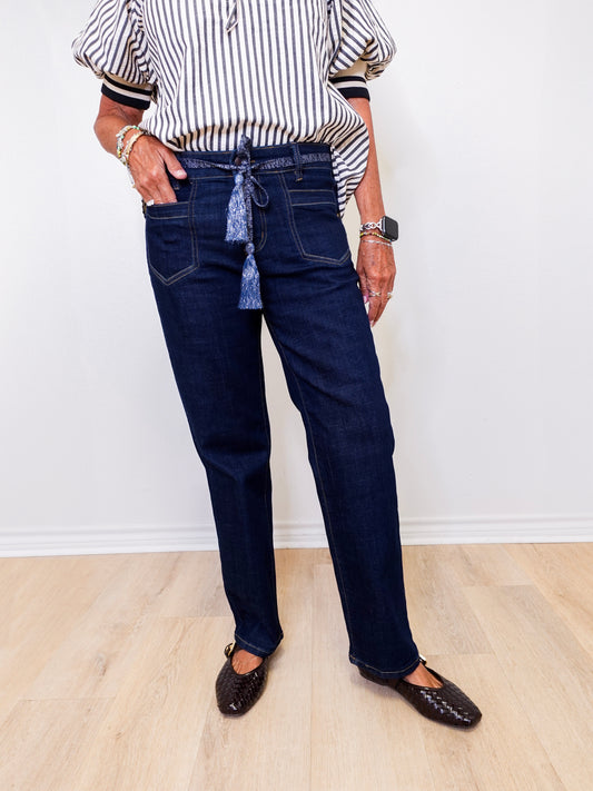 Person wearing dark blue jeans and a striped shirt against a white wall.