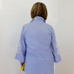 Person wearing a blue checkered shirt with floral embroidery on sleeves against a white background