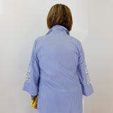Person wearing a blue checkered shirt with floral embroidery on sleeves against a white background