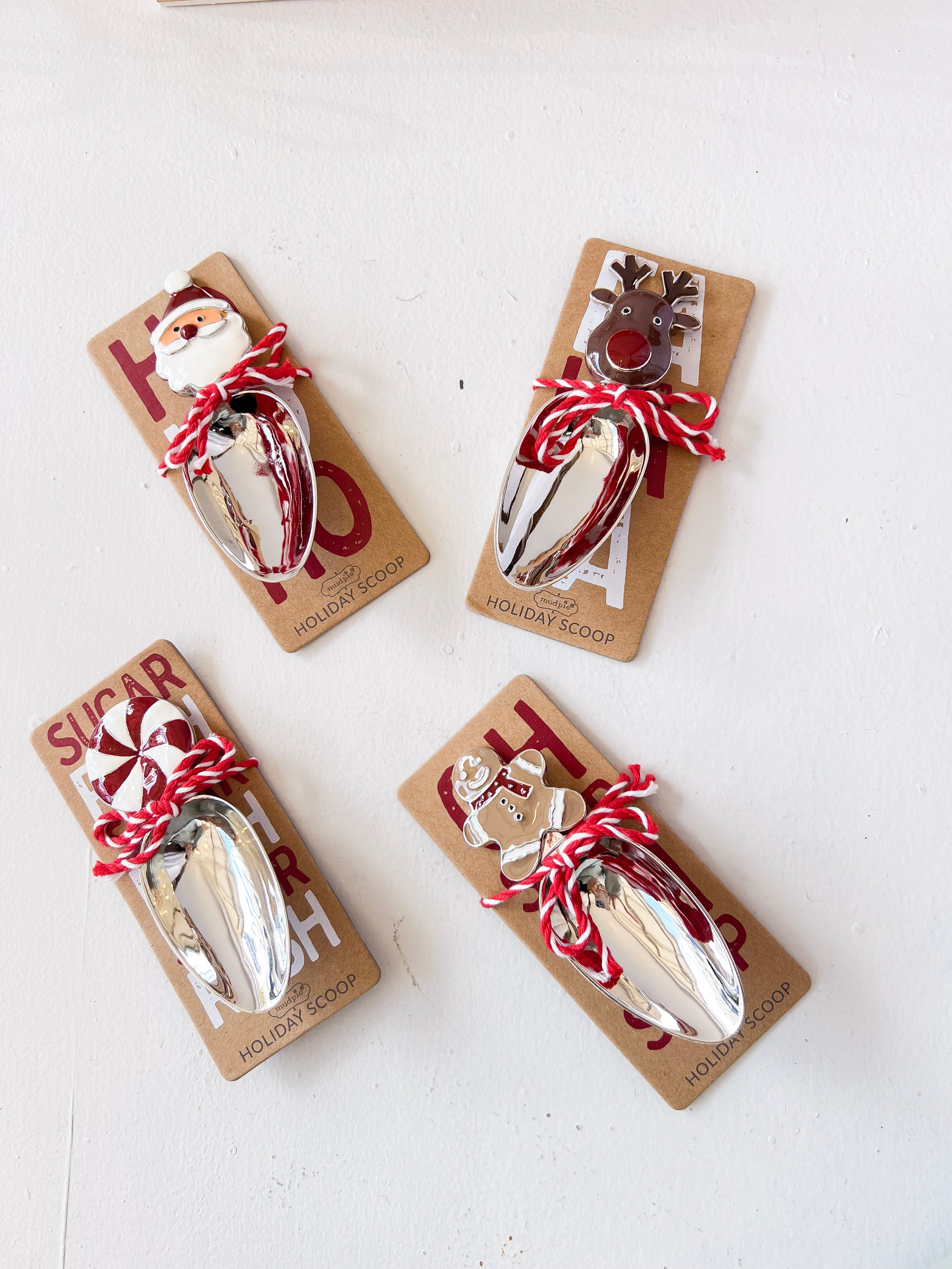 Four Christmas-themed metal spoons on packaging with Santa and reindeer designs on a white background.