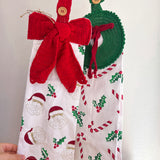 Christmas-themed kitchen towel with a red knitted bow and green knitted wreath on a white background.