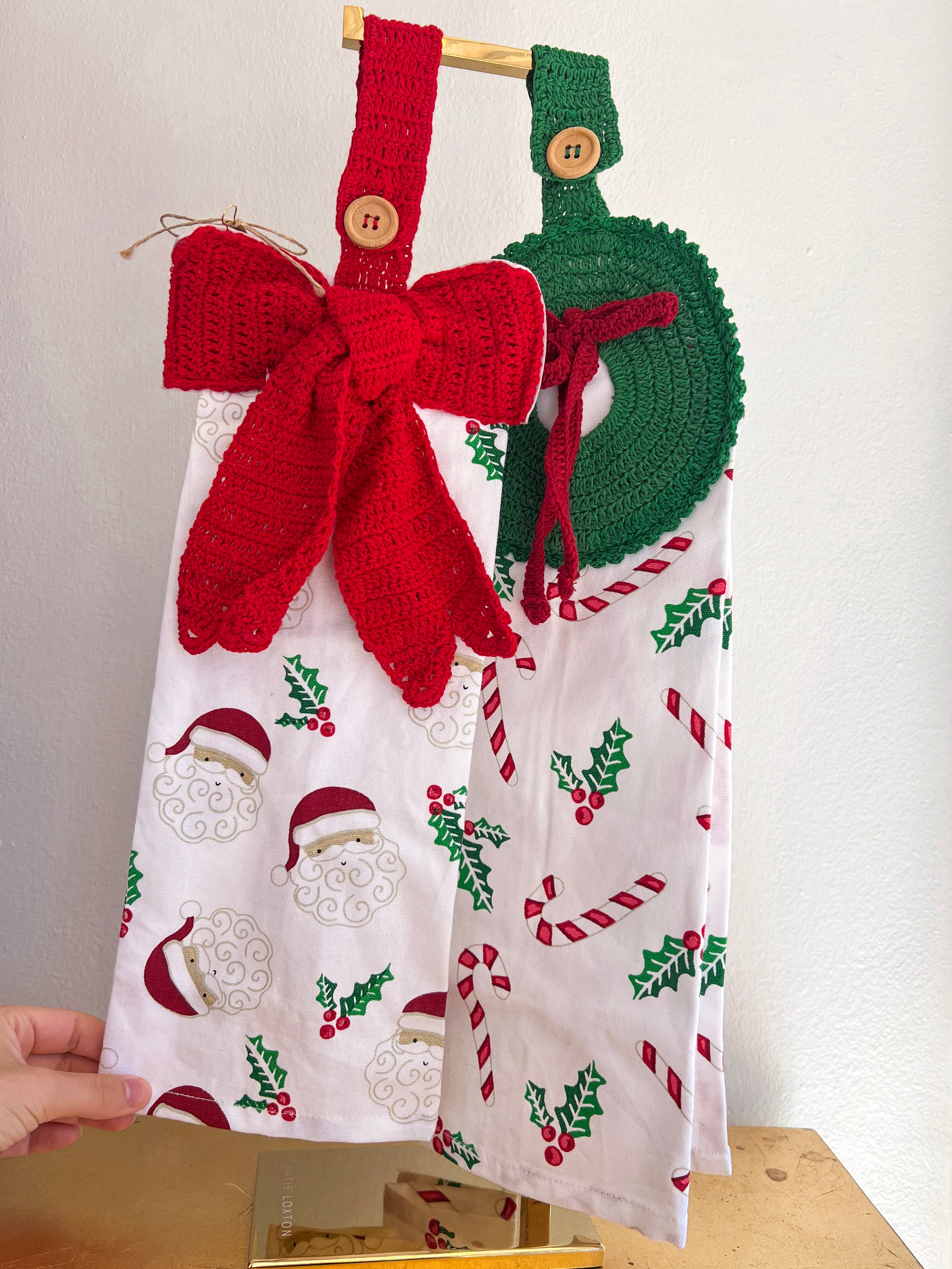 Christmas-themed kitchen towel with a red knitted bow and green knitted wreath on a white background.