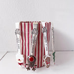 Set of Christmas-themed spoons with a striped container on a white surface.