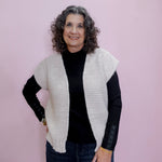 Woman wearing a white knit vest over a black long-sleeve shirt on a pink background