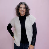 Woman wearing a white knit vest over a black long-sleeve shirt on a pink background