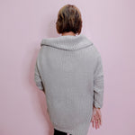 Person wearing a light gray knitted cardigan against a pink wall