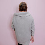 Person wearing a light gray knitted cardigan against a pink wall