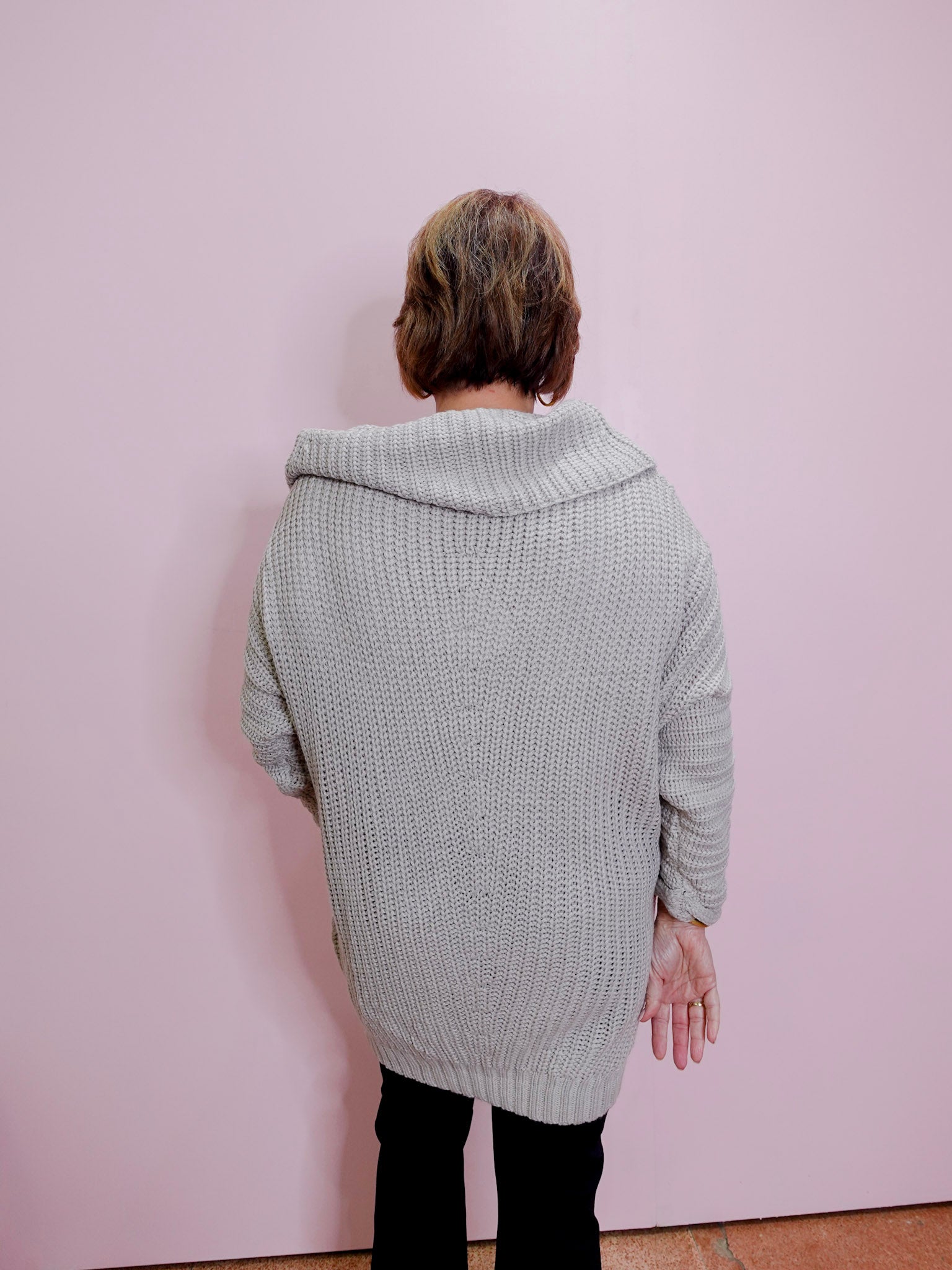 Person wearing a light gray knitted cardigan against a pink wall