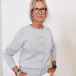 Woman wearing a gray cardigan and white pants against a plain background