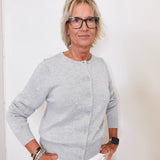 Woman wearing a gray cardigan and white pants against a plain background