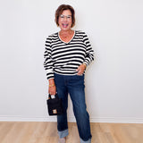 Woman wearing a black and white striped sweater and blue jeans, standing against a white wall.