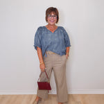 Woman wearing a blue blouse and beige pants, holding a red handbag against a white wall.