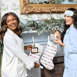 Two women in pajamas holding stockings in a decorated room with a Christmas theme.