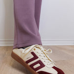 Maroon and white sneakers with brown soles worn indoors on a wooden floor.