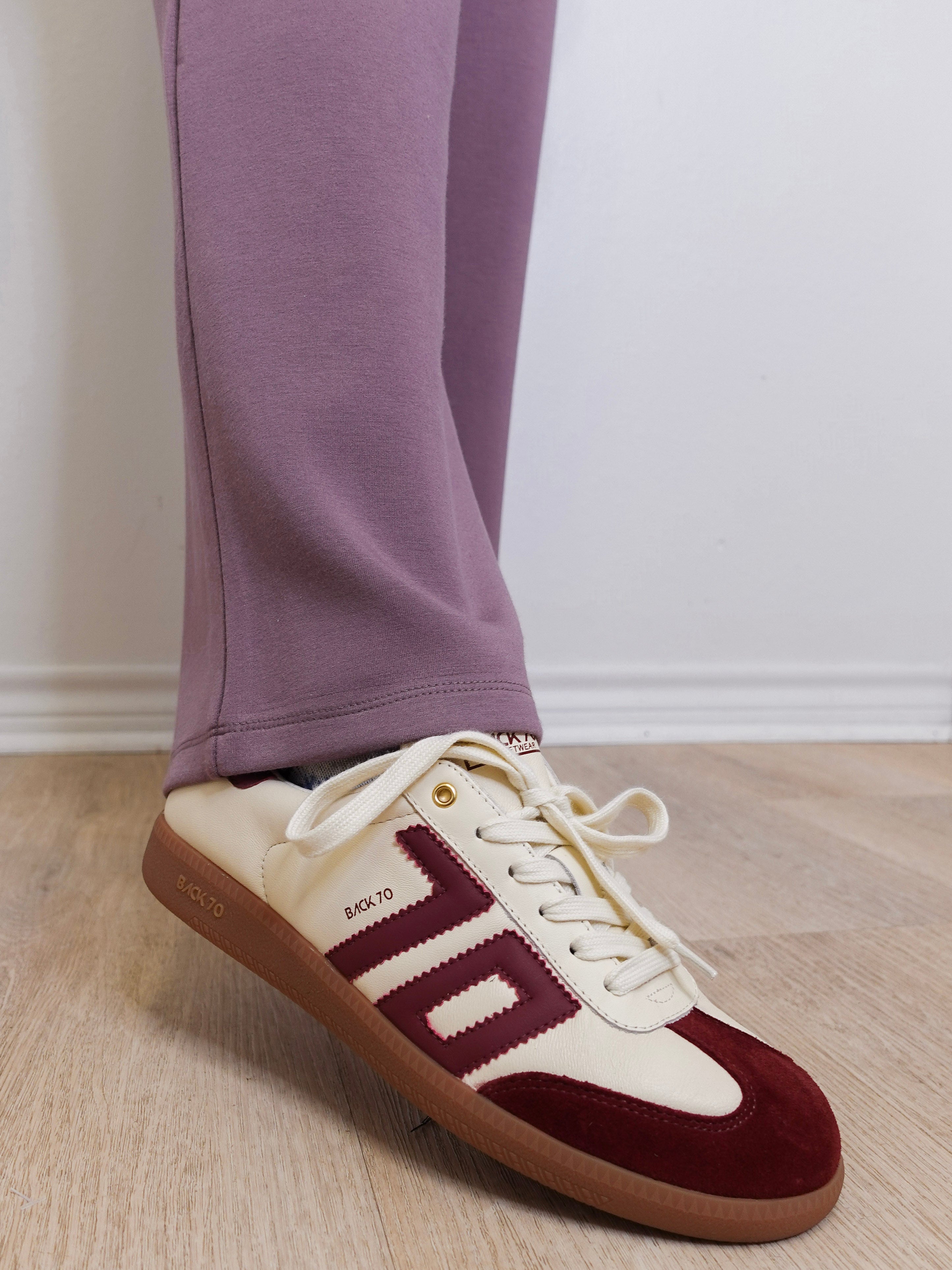Maroon and white sneakers with brown soles worn indoors on a wooden floor.