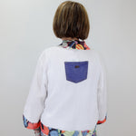 Person wearing a white shirt with a colorful pattern and a blue pocket on a plain background