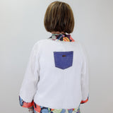 Person wearing a white shirt with a colorful pattern and a blue pocket on a plain background