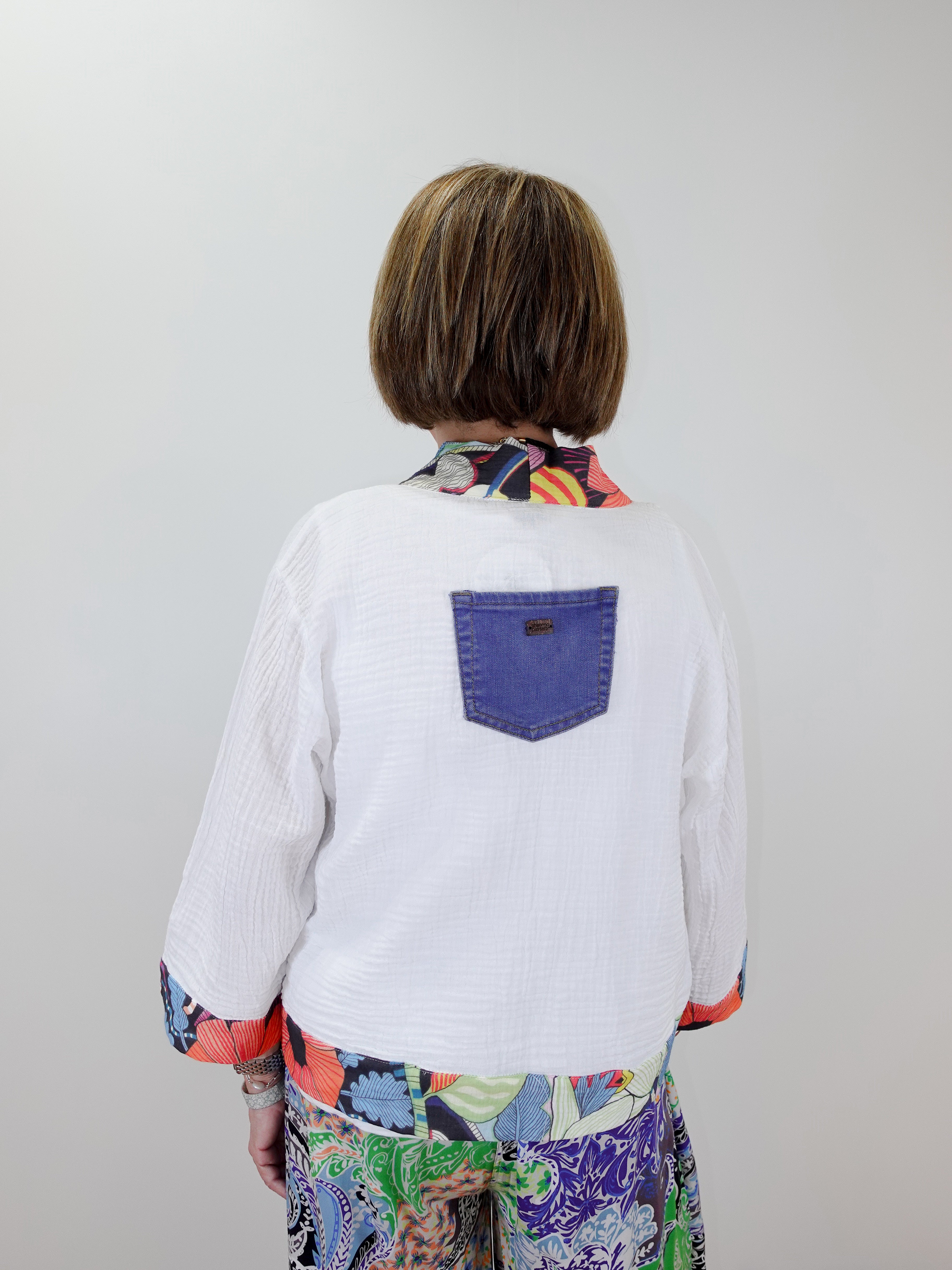 Person wearing a white shirt with a colorful pattern and a blue pocket on a plain background