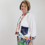 Woman wearing a colorful outfit with a white cardigan and patterned pants against a plain background