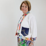 Woman wearing a colorful outfit with a white cardigan and patterned pants against a plain background