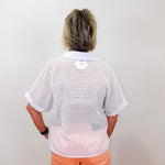 Person wearing a white open-knit shirt and orange pants against a plain background