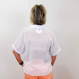 Person wearing a white open-knit shirt and orange pants against a plain background