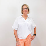 Person wearing a white shirt and peach pants against a plain background