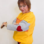 Woman wearing a yellow sweatshirt with a heart design, holding a red object against a white background