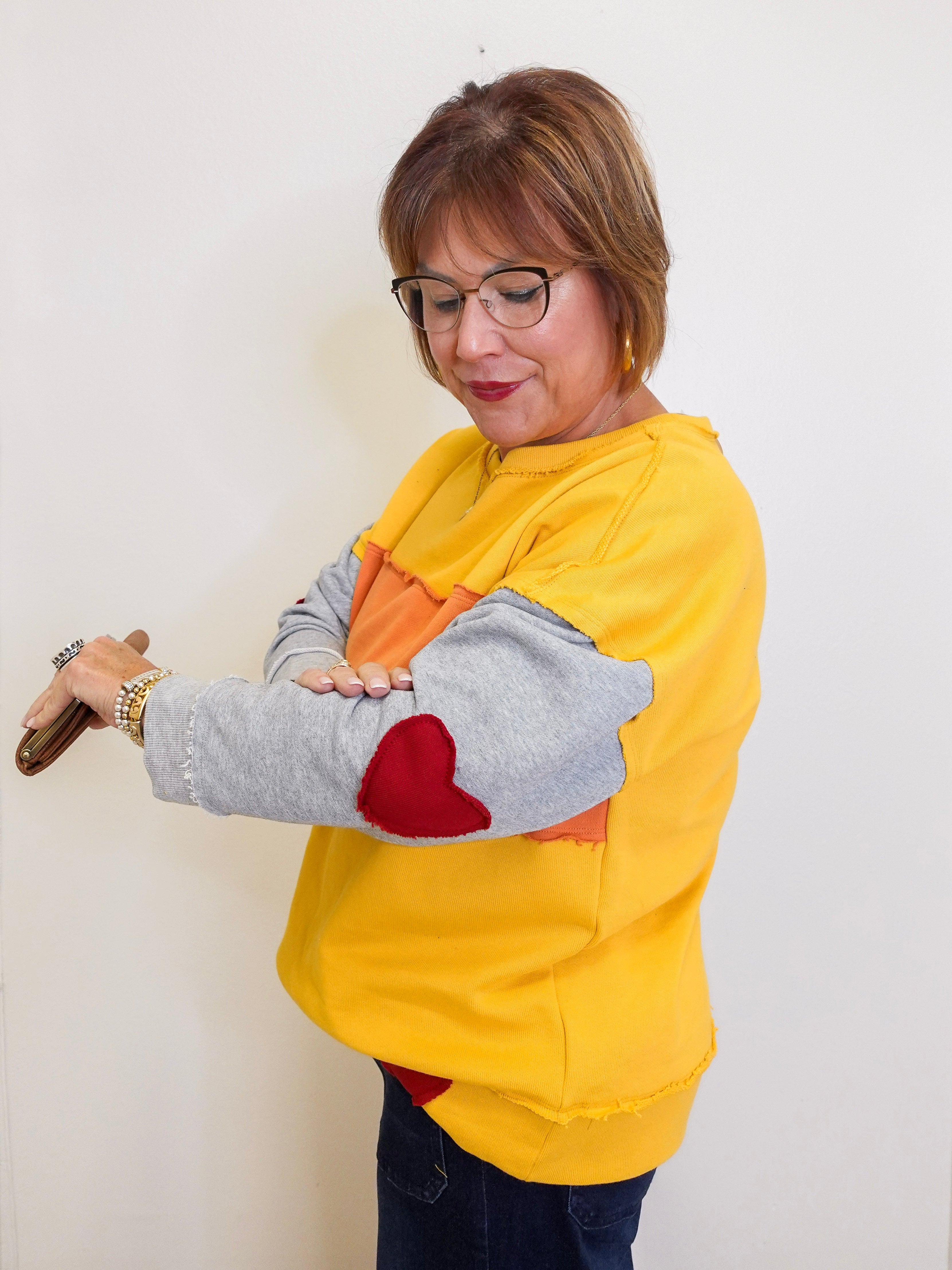 Woman wearing a yellow sweatshirt with a heart design, holding a red object against a white background