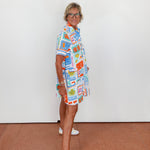 Person wearing a colorful patterned dress standing against a white wall.