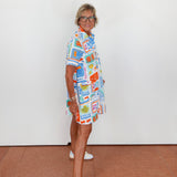 Person wearing a colorful patterned dress standing against a white wall.