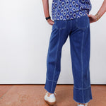 Person wearing a blue patterned shirt and blue jeans on a plain background