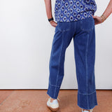 Person wearing a blue patterned shirt and blue jeans on a plain background