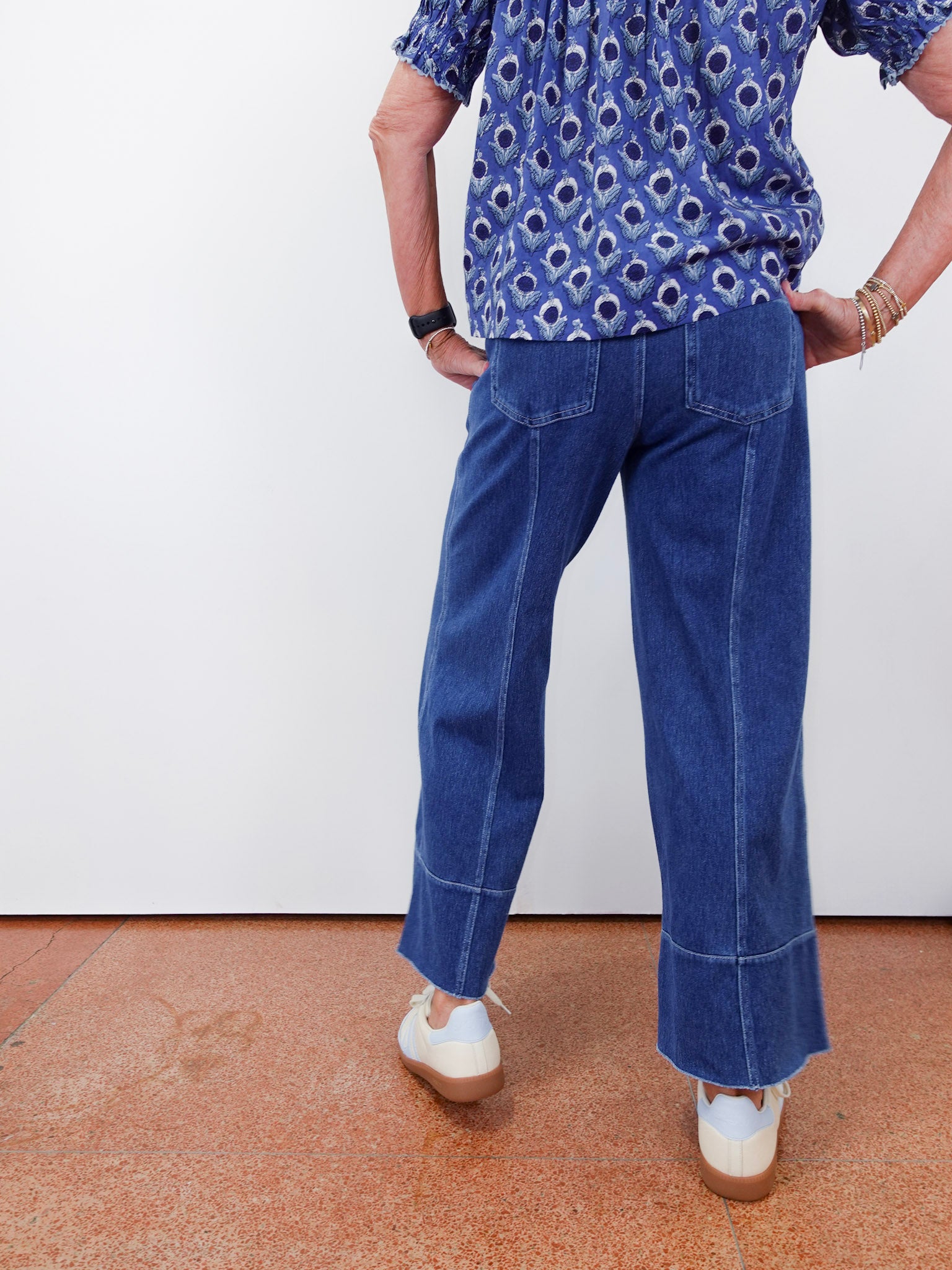 Person wearing a blue patterned shirt and blue jeans on a plain background